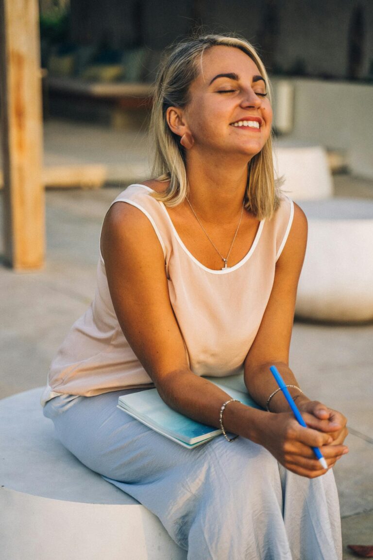 Smiling woman enjoying a peaceful moment with a notebook outdoors, symbolizing relaxation and mindfulness.